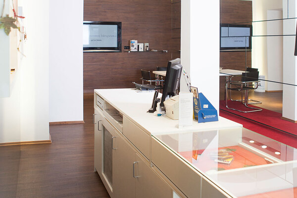 Modernes, helles Büro mit Empfangstheke, Computer, Glastheke und Besprechungsbereich.